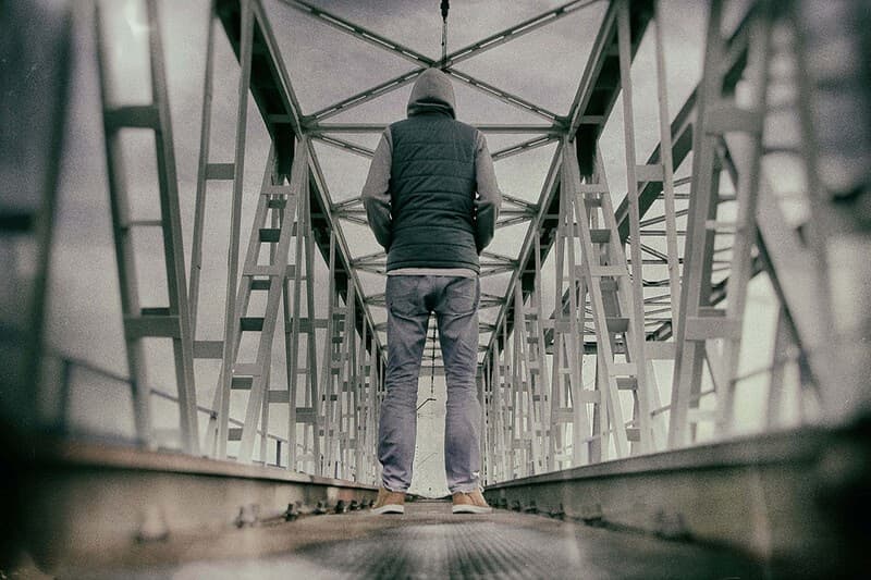 An addict stands on a walkway, contemplating making the first step of the journey to recovery.