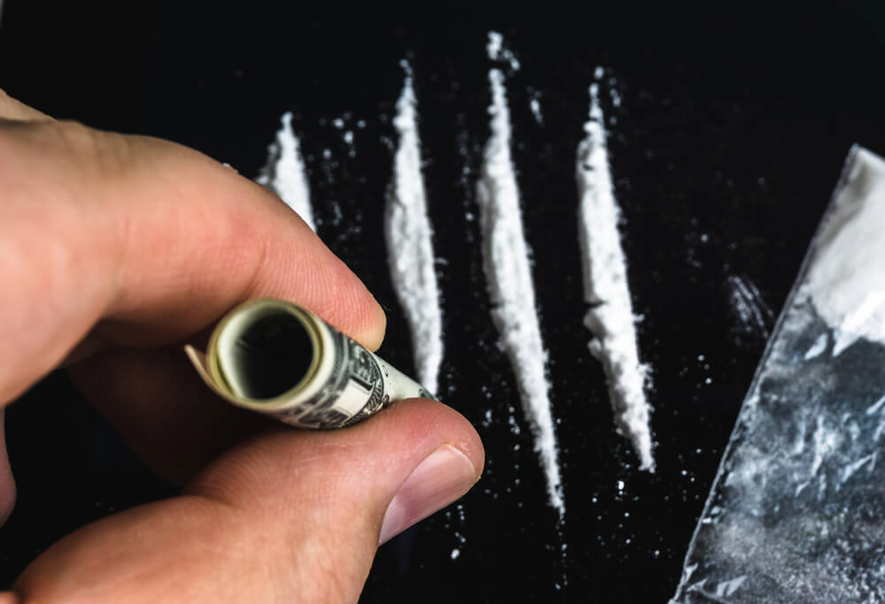 Un billet d'un dollar enroulé est utilisé par un toxicomane pour sniffer des lignes de cocaïne.